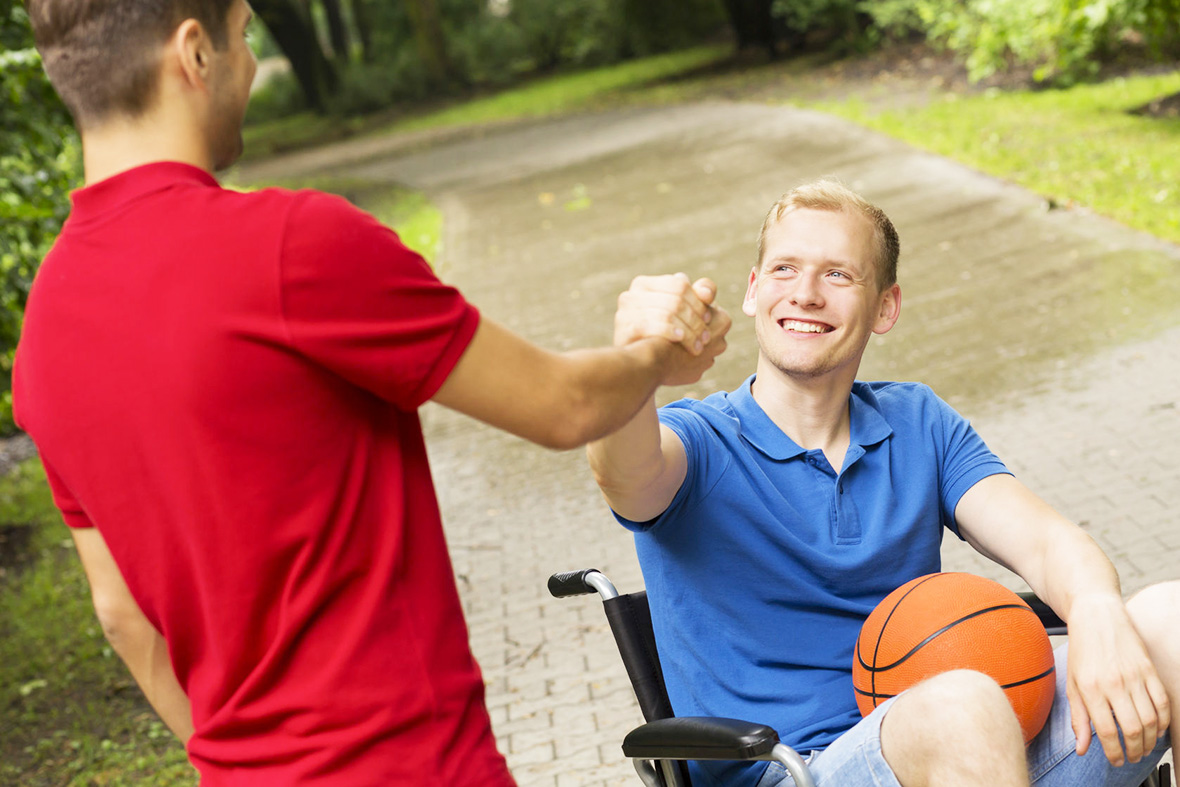 63927960 - shot of a young man in a wheelchair smiling at his friend in a park